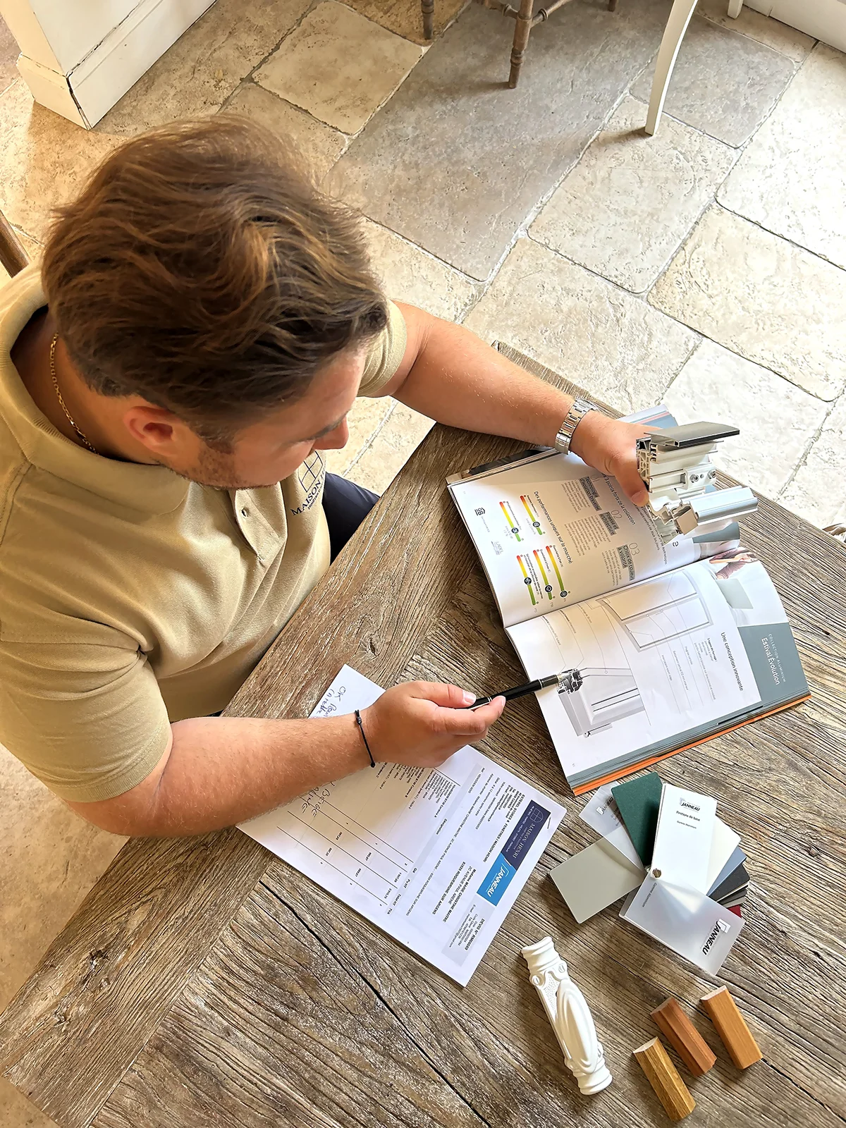 Personne consultant des documents et des échantillons de matériaux posés sur une table en bois.