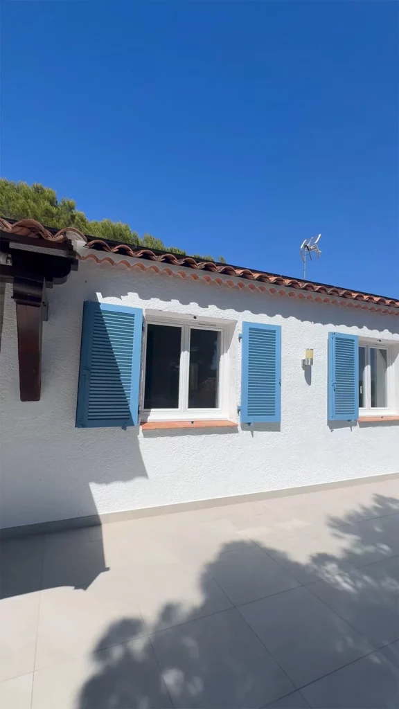 Façade blanche avec plusieurs fenêtres et volets bleus sous un ciel dégagé.